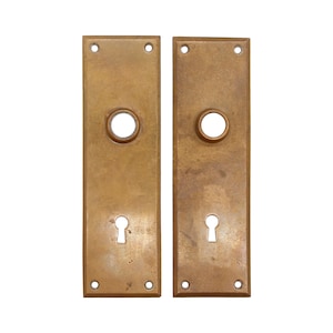 May include: Two antique brass door plates with keyholes and round holes. The plates are rectangular and have a slightly aged finish.