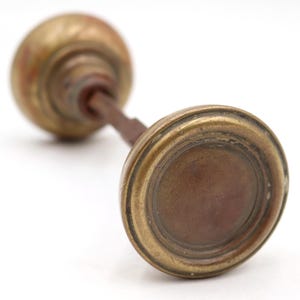 May include: Antique brass door knob with a round, aged design. The knob has a warm, golden hue with visible signs of wear, suggesting its vintage origin. The stem is a dark, rusty brown.