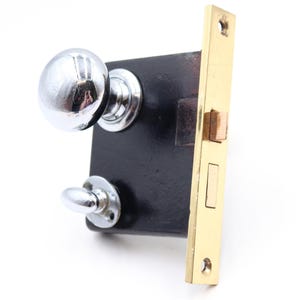 May include: A vintage door lock with a polished chrome knob and a smaller lever. The lock's body is black, and the strike plate is gold-colored. The hardware is designed for a door.