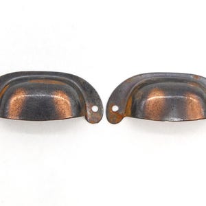 May include: Two antique-style metal drawer pulls with a copper finish. The pulls are slightly curved and have a rounded shape.