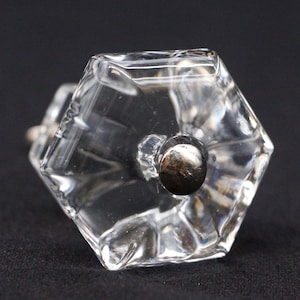 Peut inclure: Un bouton de cabinet en verre transparent de forme hexagonale avec une base en métal argenté.