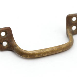 May include: A vintage brass drawer pull with a curved handle and two mounting holes on each end. The metal has a tarnished, aged appearance, suggesting it is an antique or a piece with a rustic aesthetic. The pull is set against a white background.
