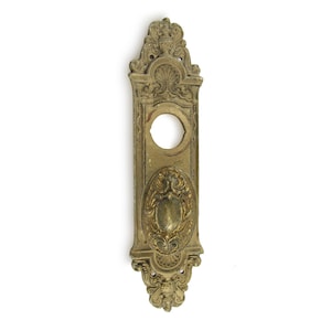 May include: Ornate gold-toned metal door plate with a decorative design and a round keyhole.