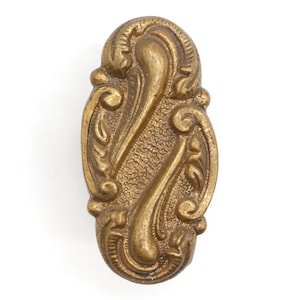 Pode incluir: Um acento decorativo de metal dourado com um design ornamentado e em espiral. O acento tem uma superfície texturizada e uma forma oval.