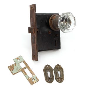 May include: Antique brass door lock set with a clear glass knob, two keyhole escutcheons, and a strike plate.