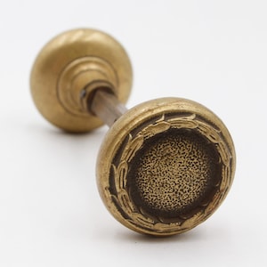 May include: Vintage brass door knob with a detailed floral design around the edge. The knob has a textured surface and a classic, vintage aesthetic. The hardware is ideal for adding a touch of elegance to any door.