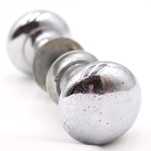 May include: A chrome door knob set with a series of round, polished knobs and washers. The metal has a reflective surface with some signs of wear, set against a white background.
