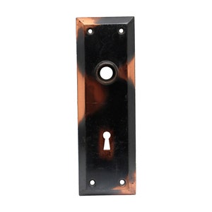 May include: A black and brown door plate with a keyhole and a round knob. The plate has a decorative pattern.