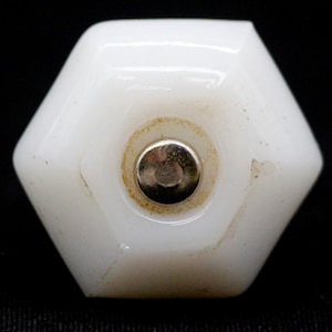 May include: White porcelain cabinet knob with a hexagonal shape and a silver metal insert in the center.