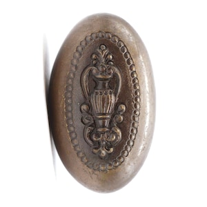 May include: An oval-shaped, antique brass door knob with an ornate design featuring a stylised vase with floral accents.