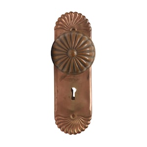 Puede incluir: Un pomo de puerta vintage de color cobre con un diseño decorativo festoneado y una cerradura. El pomo tiene un patrón circular en relieve.