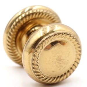 May include: A close-up of a vintage brass door knob. The knob has a round shape with a decorative rope-like edge. The brass has a warm, golden color and a slightly aged appearance.