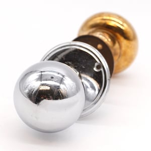 May include: A close-up of a door knob with a polished chrome finish and a brass base. The knob is disassembled, showing the inner workings.