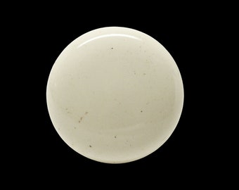 May include: A close-up of a round, off-white, textured surface with a slight sheen. The surface has a few small, dark brown spots.