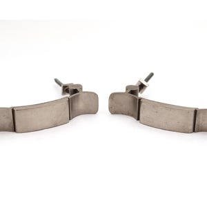 Puede incluir: Dos tiradores de armario de metal cepillado con tornillos de montaje. Cada tirador se compone de tres secciones rectangulares y extremos curvos. Los tiradores se muestran sobre un fondo blanco.
