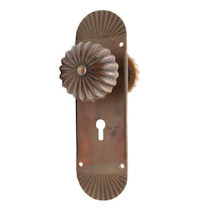Può includere: Maniglia per porta antica in bronzo con pomello scanalato a forma di fiore e buco della serratura. La placca posteriore presenta un motivo decorativo a ventaglio. Ferramenta vintage.