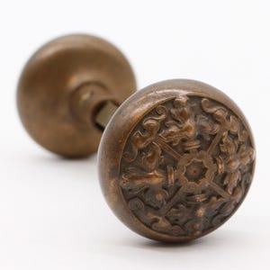 May include: A vintage brass door knob with an ornate design featuring a central rosette and four stylised floral motifs.