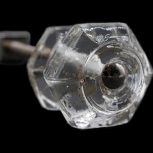 Puede incluir: Un pomo de puerta de vidrio transparente con forma hexagonal y un tornillo de metal.