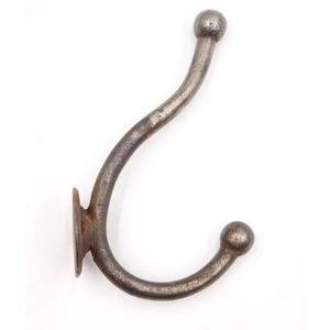 May include: A dark gray metal wall hook with a weathered, textured finish. The hook features a curved, double-pronged design with a rounded ball tip on each end and a flat, circular mounting plate at the base for attachment to a vertical surface.