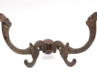 Può includere: Gancio da parete in stile antico con finitura bronzo. Il gancio presenta un design curvo con volute decorative e accenti floreali. È progettato per il montaggio a parete ed è probabilmente realizzato in metallo.