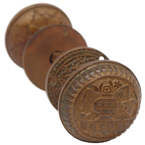 Könnte beinhalten: Antiker Türknauf aus Messing mit aufwendigen floralen und geometrischen Mustern. Der Knauf hat ein erhabenes, kreisförmiges Design mit einem zentralen Blumenmotiv.