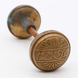 May include: A pair of antique brass door knobs with intricate floral designs. The knobs are round and have a raised center with a sunburst pattern.