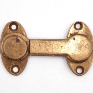 May include: A vintage brass door latch with an oval shape on each end and a rectangular connecting bar. Each oval end has two screw holes and a circular raised section. The brass has a worn, aged appearance.