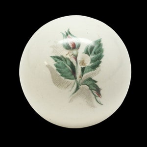 May include: White ceramic knob with a green and white floral design. The flower is a white rose with green leaves.