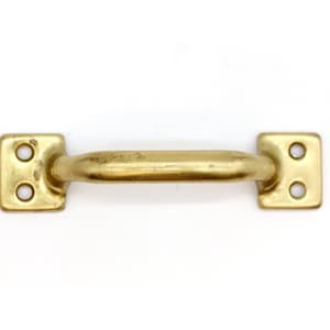 Könnte beinhalten: Ein goldfarbener Metall-Schrankgriff mit abgerundeter rechteckiger Form und zwei Löchern zur Befestigung.