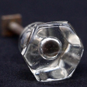 Könnte beinhalten: Ein klarer Glas-Türknopf mit einem silbernen Metallsockel. Der Knopf hat eine sechseckige Form mit abgerundeten Kanten.