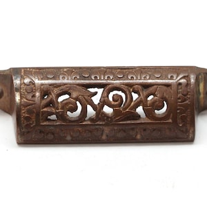 May include: A vintage, ornate, cast iron drawer pull with a decorative, openwork design. The pull is a dark bronze color and has two holes for mounting.
