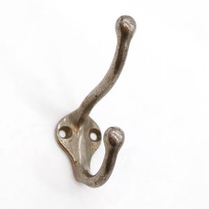 May include: A silver metal double hook with rounded ends. The hook is mounted on a flat, oval-shaped base with two screw holes.