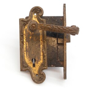 May include: Antique brass door handle and lock with ornate details. The handle has a decorative knob and a long, curved lever. The lock has a keyhole and a visible mechanism.