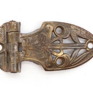 May include: Antique brass hinge with an ornate, decorative design. The hinge has a leaf-like pattern and is in good condition.