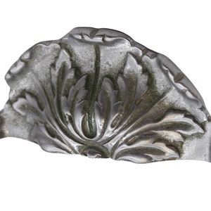 May include: A silver-coloured metal decorative piece with a floral design. The piece is shaped like a half-circle and has a raised, ornate design.