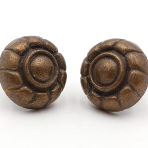 Puede incluir: Dos tiradores de armario antiguos de color bronce. Cada tirador es redondo con un diseño circular central rodeado por un patrón texturizado en forma de pétalo. Estos tiradores son probablemente para muebles o decoración.