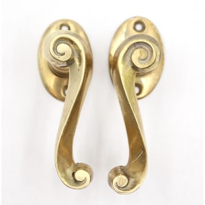 May include: Pair of antique brass door handles. Each handle features an oval backplate and a curved lever with a decorative spiral design. The handles are a warm, aged brass color, suggesting vintage or retro style.