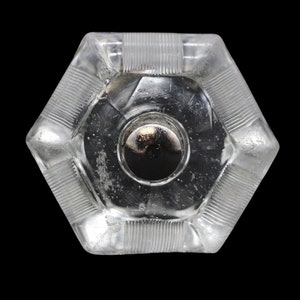 Op de afbeelding: Een zeshoekige flesstopper van helder glas met een zilveren metalen bovenkant. De stopper heeft een getextureerd ontwerp rond de randen.