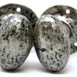 May include: Two antique silver door knobs with a distressed finish. The knobs are oval shaped and have a circular base with three holes.