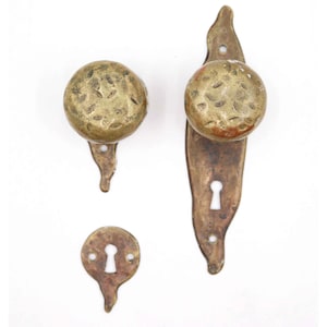 May include: Antique brass door hardware set. Includes a door knob, a long escutcheon with a knob, and a small escutcheon. The hardware has a hammered texture and a warm, aged patina. Perfect for vintage or rustic decor.
