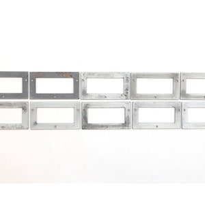 May include: Ten silver metal rectangular frames with rounded corners and small holes in each corner. The frames are arranged in two rows of five.