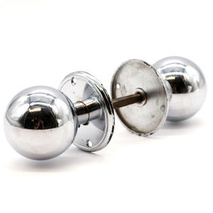 May include: A pair of chrome door knobs with round handles. The knobs are attached to a metal plate with screws.