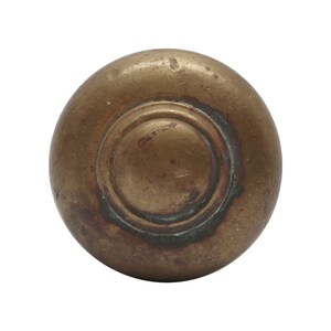 May include: A round, brass door knob with a raised, circular design in the center.