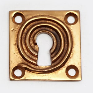 May include: A square brass keyhole cover with a spiral design and four mounting holes.
