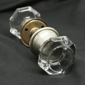 May include: A clear glass door knob with a brass base and a silver-coloured ring around the knob.