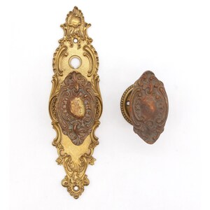 May include: A set of two antique brass door knobs with ornate floral designs. The knobs are in a worn, aged condition, giving them a vintage aesthetic.