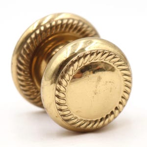 Könnte beinhalten: Ein Paar antike Türknöpfe aus Messing. Jeder Knopf ist rund mit einem dekorativen, seilartigen Rand. Die Knöpfe haben eine polierte Oberfläche und sind vor einem weißen Hintergrund platziert. Diese Knöpfe sind für Innentüren geeignet.