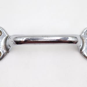 May include: A shiny, chrome-plated cabinet pull handle. The handle is a straight bar with rounded ends, each featuring two screw holes. The hardware is designed for easy installation and adds a touch of vintage charm.