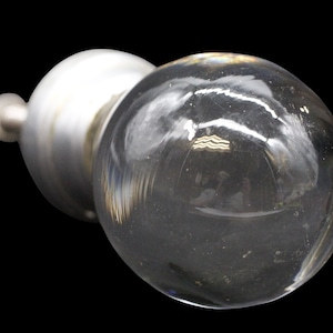 May include: A clear glass cabinet knob with a silver metal base. The knob is round and has a smooth surface.
