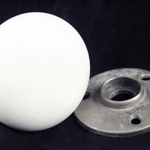 Könnte beinhalten: Ein glatter, kugelförmiger weißer Knauf gepaart mit einer kreisförmigen, metallisch grauen Montageplatte mit drei vorgebohrten Schraublöchern. Das Beschlagteil ist für die Befestigung an einer Oberfläche konzipiert und weist ein sauberes, abgerundetes Profil sowie eine flache Grundplatte im Industriestil auf.